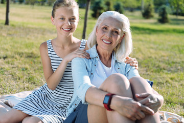 Family members. Joyful positive nice girl holding her grandmothers shoulders and smiling while spending time together