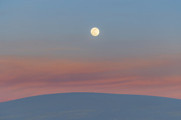 A super moon rises over sand dunes and the remnants of sunset lit clouds - 191362120