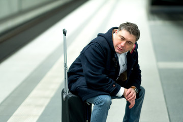 Traveler sitting on his suitcase waiting for a delayed train at railway station platform