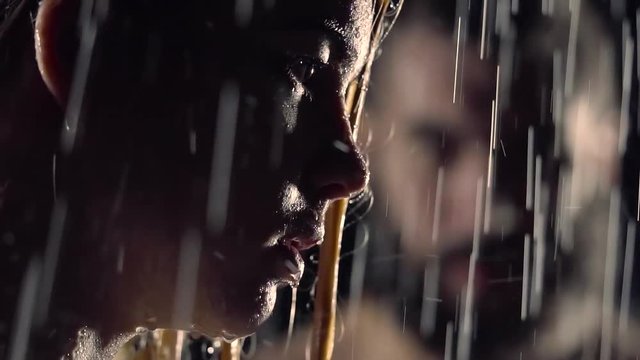 Side view shot of a seductive blonde woman standing under the heavy rain.
