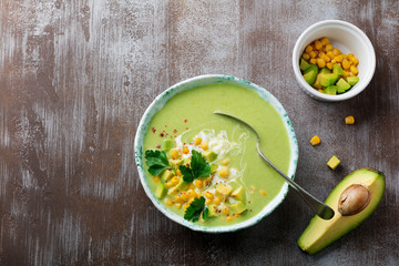 Homemade tender soup puree from avocado and corn with cream in rustic ceramic plate on gray concrete old background. Selective focus. Top view. Copy space.