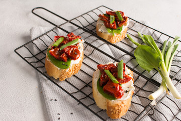 Roasted cherry tomatoes bruschetta with mozzarella, sorrel, onion and black sesame on light grey concrete background. Selective focus, close up.