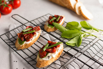 Roasted cherry tomatoes bruschetta with mozzarella, sorrel, onion and black sesame on light grey concrete background. Selective focus, close up.