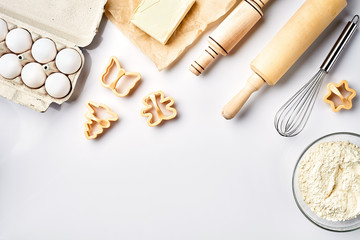 Bowl with wheat flour, rolling pin, whisk, eggs, butter, cookie cutters. Top view on a white table with a copy space