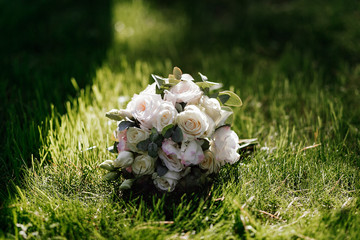Obraz na płótnie Canvas Wedding bouquet of cream and white roses lies on the grass in the sunlight