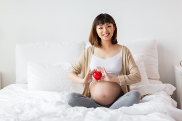 Obraz na płótnie Canvas happy pregnant asian woman with red heart in bed