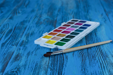 Watercolor paint and brushes on blue wooden background