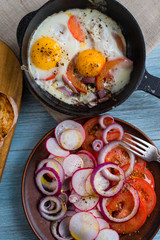 Fried eggs with tomatoes and spring salad with radishes and onions - rustic lunch