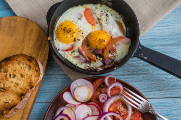 Fried eggs with vegetables, salad and toast bread on a wooden background - top view