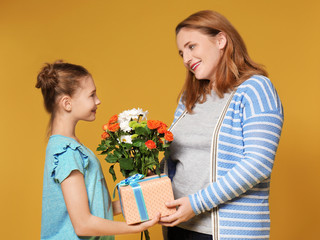 Cute little girl giving her mother present and flowers on color background