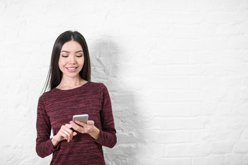 Beautiful young woman with mobile phone near white wall