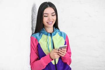 Beautiful young woman with mobile phone near white wall