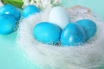 Decorative nest with dyed Easter eggs on table, closeup
