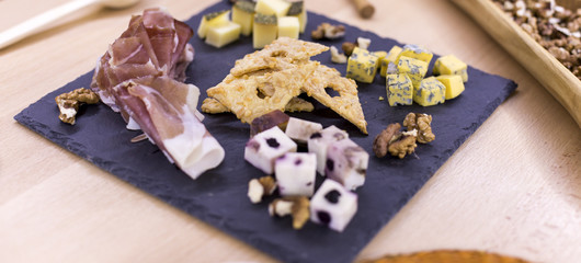 Different types of cheese and nuts on a black cutting board