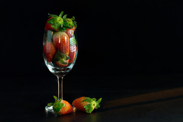 Strawberries in glass cup and fall out of cup on dark floor and dark background with streamer light