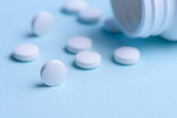 White round pills and pill bottle on blue background