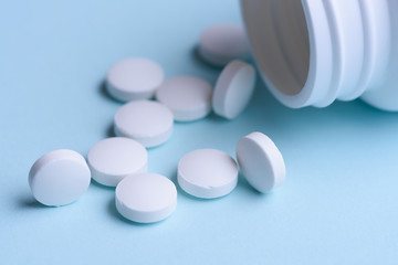 White pills and pill bottle on blue background