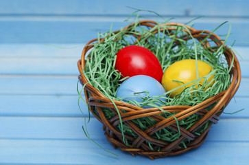 Easter basket filled with colorful eggs on a blue wooden background