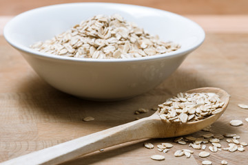 white bowl of oat flakes wooden spoon on wood table