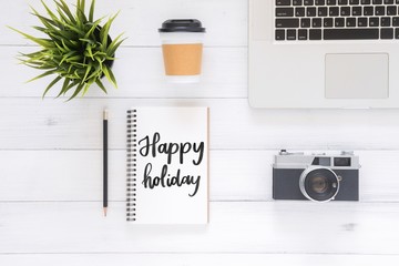 Minimal Work space - Flat lay view photo of working desk with happy holiday wish notebook, coffee cup, camera and laptop on white wooden background. Top View flat lay photography New year 2018 concept