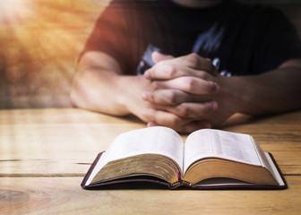 A man praying to God with open bible on wooden table 