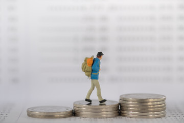 Business , travel and money concept. Traveler miniature figure with backpack walking on stack of...