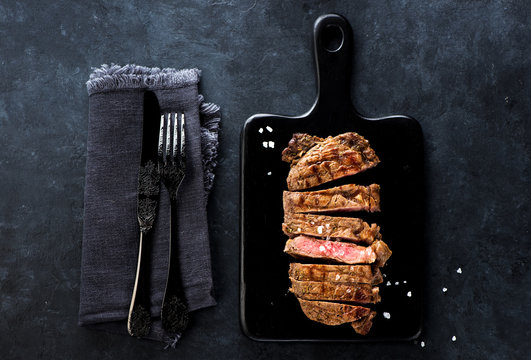 Slices beef Steak Ribeye on a black cutting board on a dark concrete background