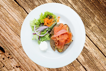 Baked potatoes with salmon, mixed salad and cheese on wooden board, top view