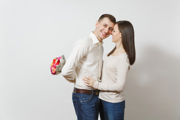 Couple in love. Woman looking behind man who hiding behind him bouquet of beautiful roses flowers isolated on white background. St. Valentine's Day, International Women's Day birthday holiday concept