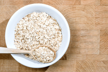 white bowl of oat flakes wooden spoon on wood table