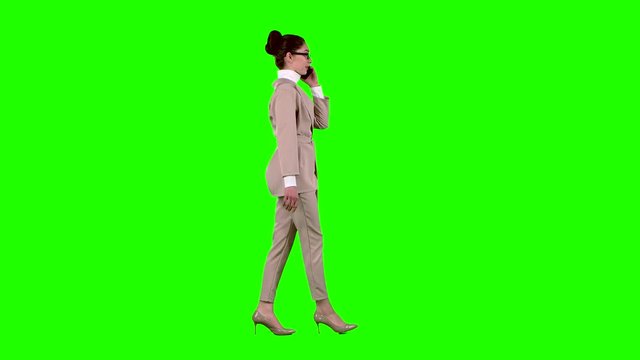 Woman is walking and talking on the phone. Green screen. Side view. Slow motion