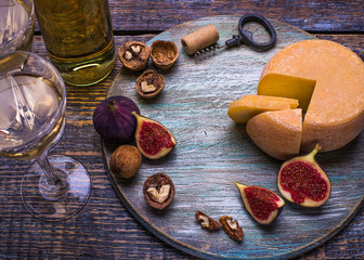 White wine in a bottle, cork, bottle screw and a set of products - cheese, grapes, nuts, olives, figs on a wooden board, background