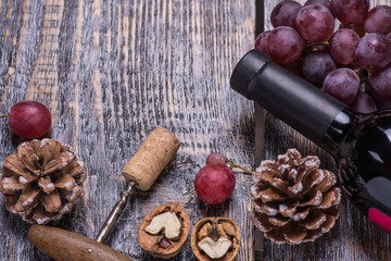 Red wine in a bottle, cork, bottle screw and a set of products - grapes, nuts on a wooden board, background