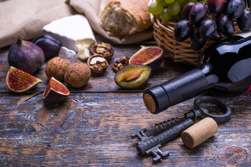 Red wine in a bottle, cork, bottle screw and a set of products - cheese, grapes, nuts, olives, figs on a wooden board, background