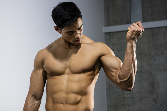 An Asian fitness model flexing his bicep muscle and looking at it.