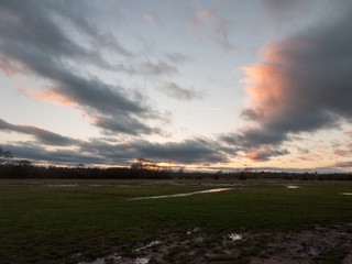 sunset moody sky winter autumn over green field with trees water