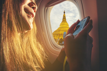Woman sitting by aircraft window and using a digital mobile during the flight. Yangon, Myanmar...