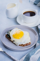 Rye bread toasts with fried spinach and egg with cup of coffee and milk on blue table background. Healthy Breakfast Food Concept.