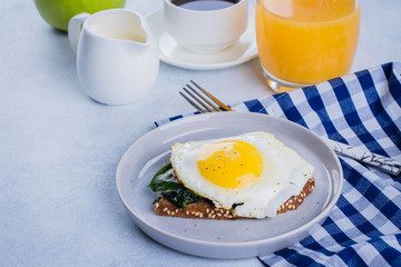 Rye bread toasts with fried spinach and egg with cup of coffee and orange juice on blue table background. Healthy Breakfast Food Concept. Copy Space
