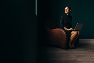 Thoughtful lady sitting on armchair with laptop