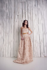 Brunette girl in long evening dress and with professional make-up and hairstyle stands elegantly on the background with white wooden texture