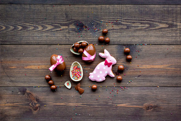 Easter composition. Easter sweet gift. Chocolate eggs near cookies in shape of Easter bunny on dark wooden background top view space for text