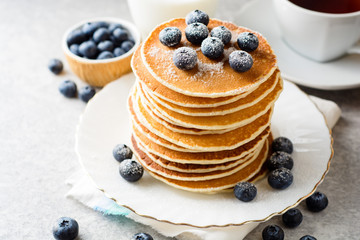 Pancakes with blueberries and sugar on grey stone background.