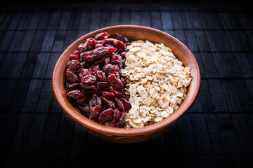 Raw oatmeal with dried cranberries in a round clay bowl on a dark wooden background. Healthy fitness vegetarian breakfast granola meal with cranberries. Selective focus