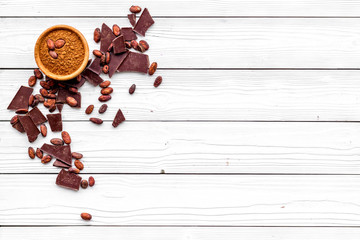 Chocolate and cacao concept. Cocoa powder in bowl near cocoa beans and broken chocolate on white background top view copy space