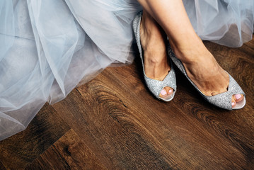 Bride's legs in chick silver shoes on wooden floor