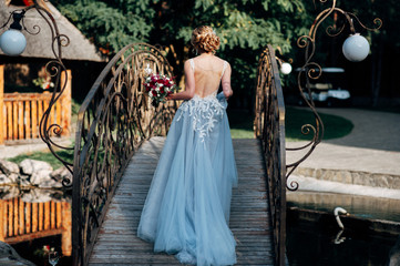 Bride is walking across bridge in grey wedding dress with naked back