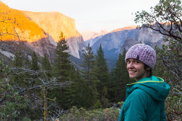 Naklejka premium Young caucasian woman in winter clothing poses at sunset under half dome in Yosemite valley