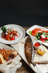 grilled mackerel and sea bass. Salad of fresh vegetables. Serving on a wooden Board on a rustic table. Barbecue restaurant menu, a series of photos of different meats anf fish