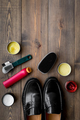 Shoe polish, brushes, wax near black shiny leather shoes on dark wooden background top view copy space